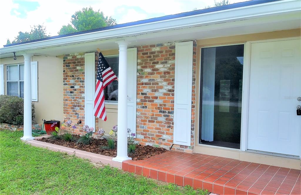 The exterior of a house features a brick facade, white columns, and a tiled porch — 641 MERRIMAC STREET, DELTONA, FL