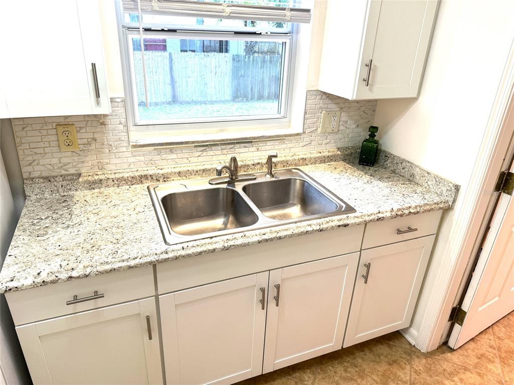 A kitchen sink with granite countertops and white cabinets sits below a window — 641 MERRIMAC STREET, DELTONA, FL