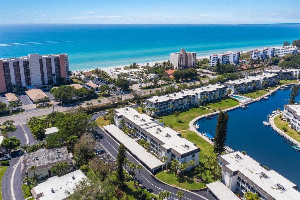 An aerial view shows a multi-story apartment complex situated along a canal near the beach — 4380 EXETER DRIVE UNIT H202, LONGBOAT KEY, FL
