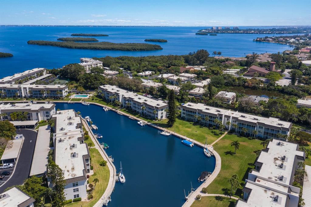 An aerial view shows a residential complex with white buildings surrounding a narrow blue canal — 4380 EXETER DRIVE UNIT H202, LONGBOAT KEY, FL