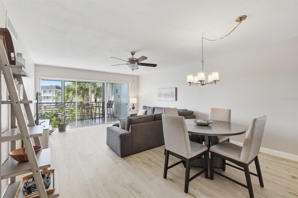 A living and dining area with light wood floors, a gray sofa, and a balcony — 4380 EXETER DRIVE UNIT H202, LONGBOAT KEY, FL