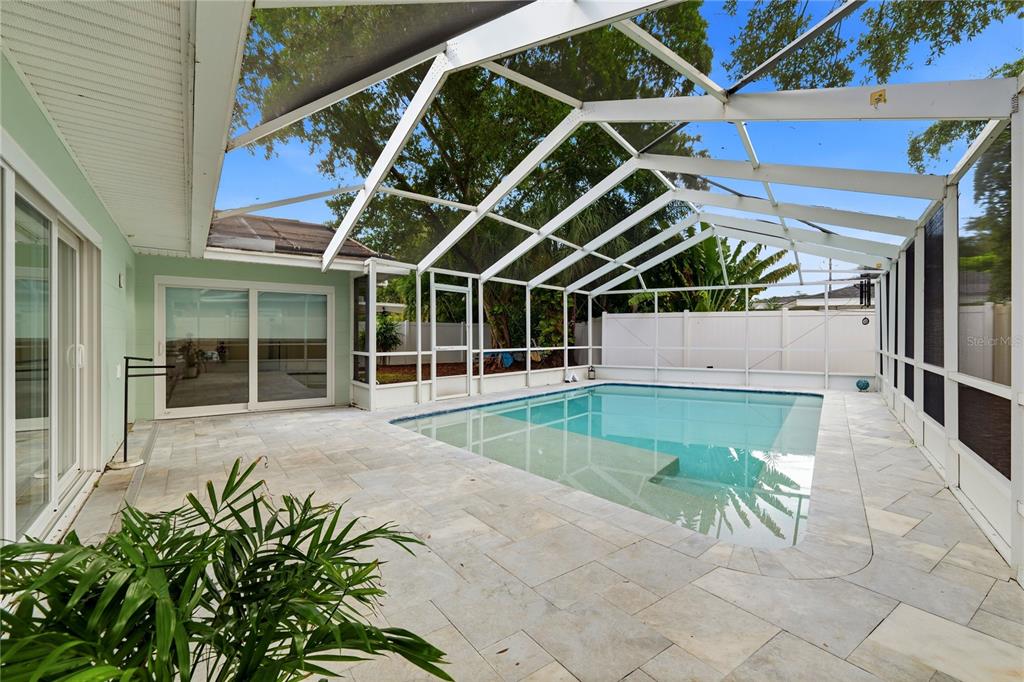 A screened-in swimming pool patio features light-colored stone pavers and a white aluminum frame enclosure — 4411 15TH STREET N, ST PETERSBURG, FL
