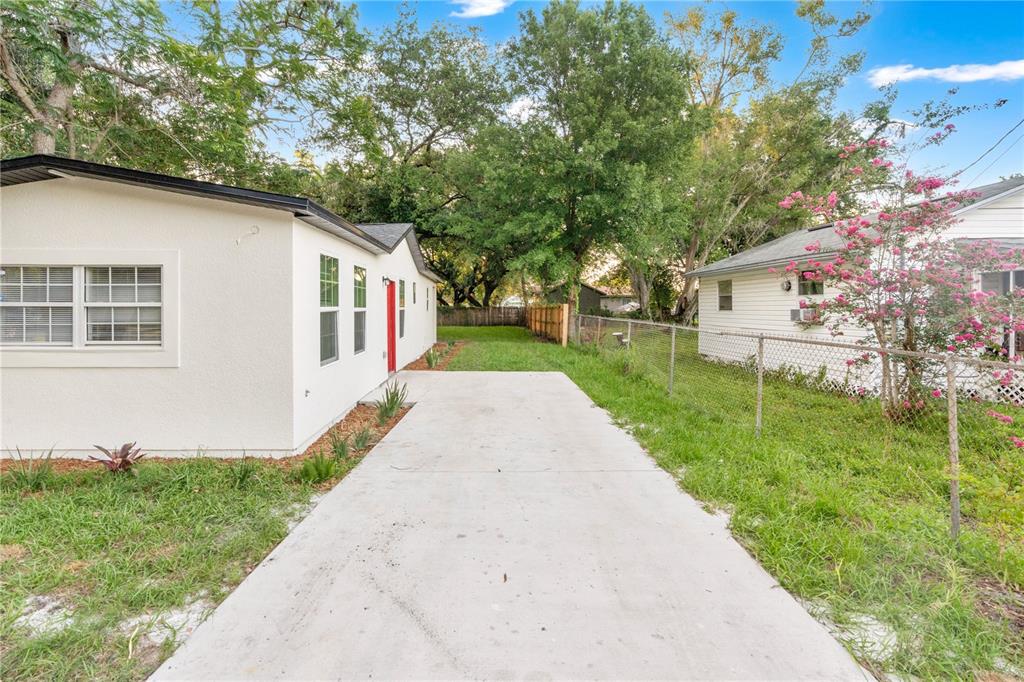 A concrete driveway leads to the side entrance of a white house with a red door — 1701 E BAY STREET, WINTER GARDEN, FL