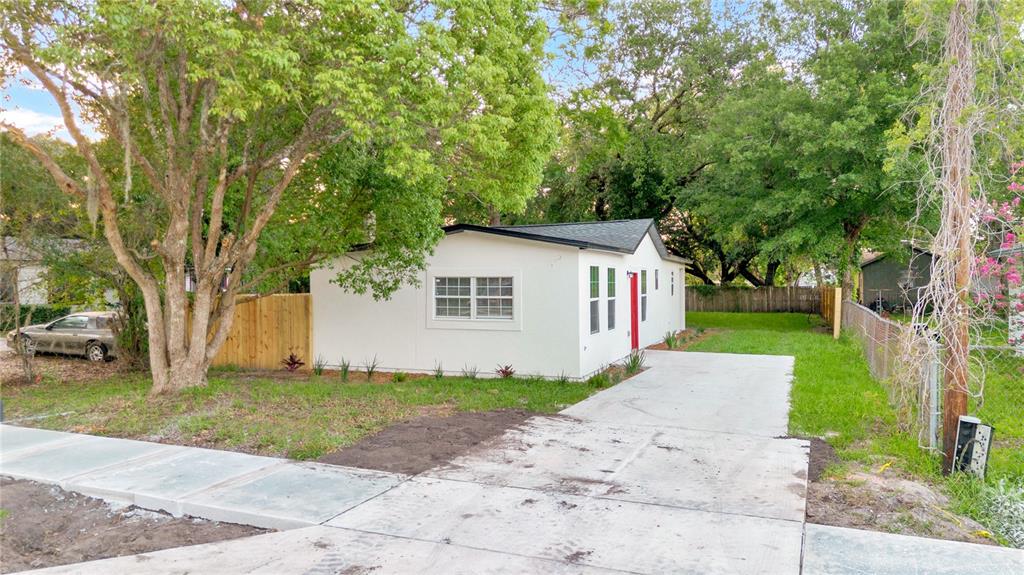 A white single-story house with a red door and a concrete driveway sits among trees — 1701 E BAY STREET, WINTER GARDEN, FL