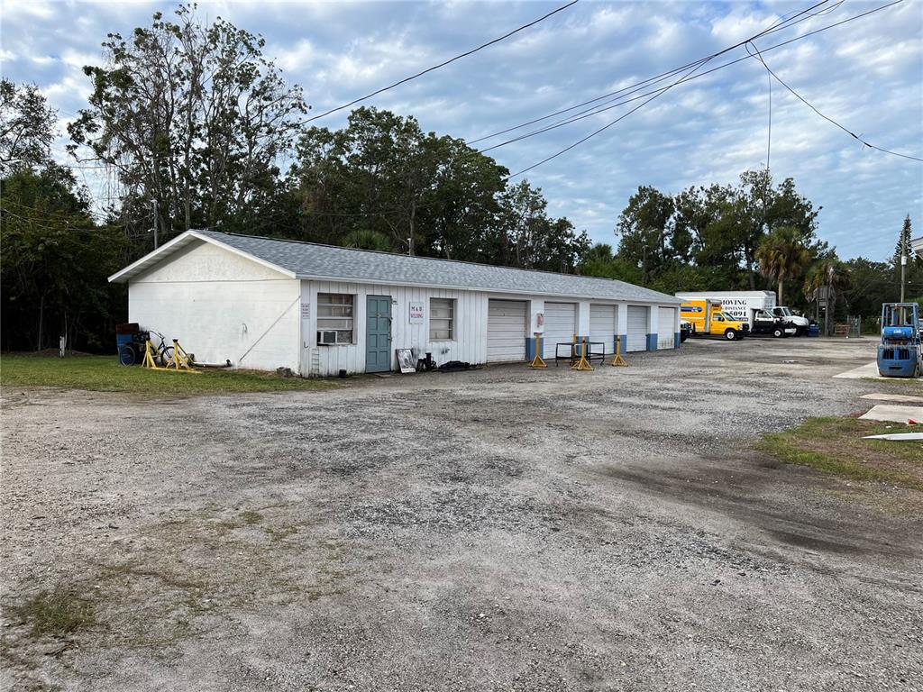 A long, white, single-story commercial building with multiple garage doors sits on a gravel lot — 14602 MARINA DRIVE, HUDSON, FL