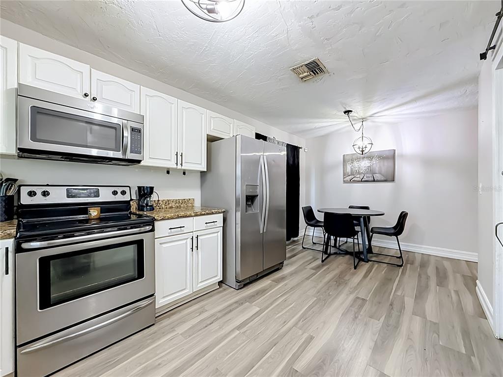 A kitchen with white cabinets, stainless steel appliances, and a small dining area with wood flooring — 8320 43RD WAY N, PINELLAS PARK, FL