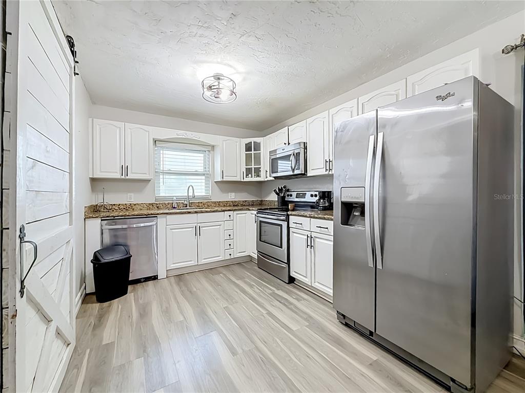 A kitchen features white cabinets, granite countertops, stainless steel appliances, and light wood-look flooring — 8320 43RD WAY N, PINELLAS PARK, FL
