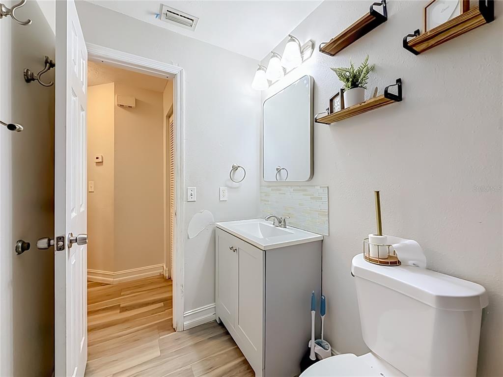 A bathroom features a gray vanity, a rectangular mirror, floating shelves, and wood-look flooring — 8320 43RD WAY N, PINELLAS PARK, FL