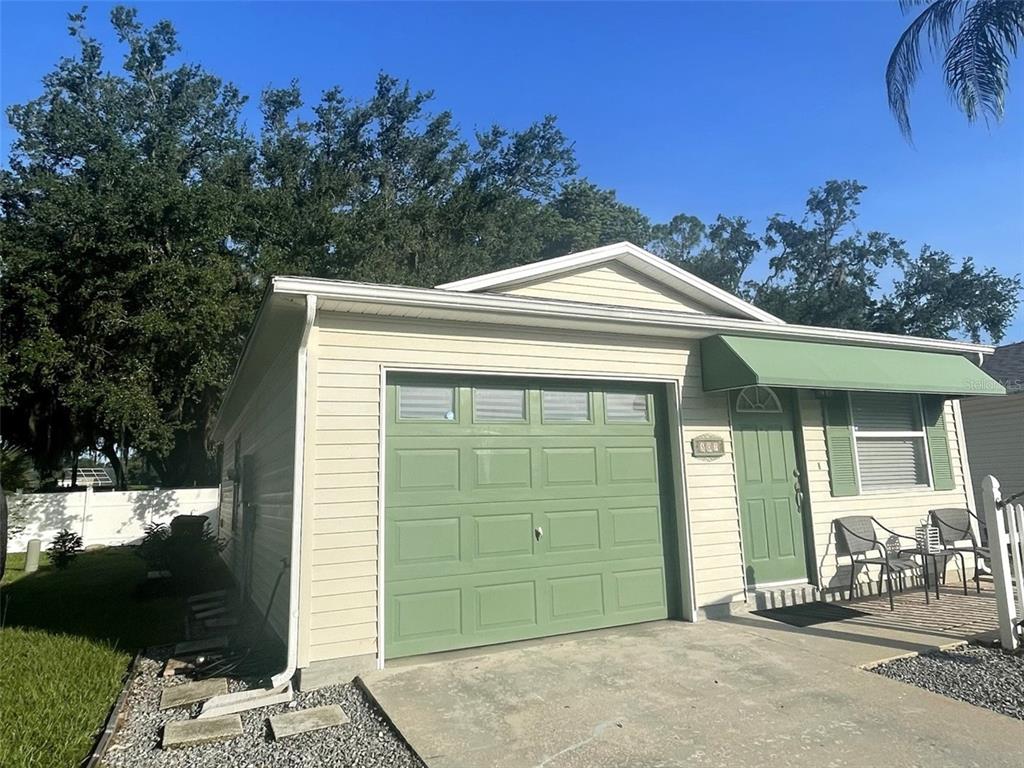 A beige house exterior features a green garage door, a matching green front door, and shutters — 507 COTTAGE PARK LANE, LEESBURG, FL