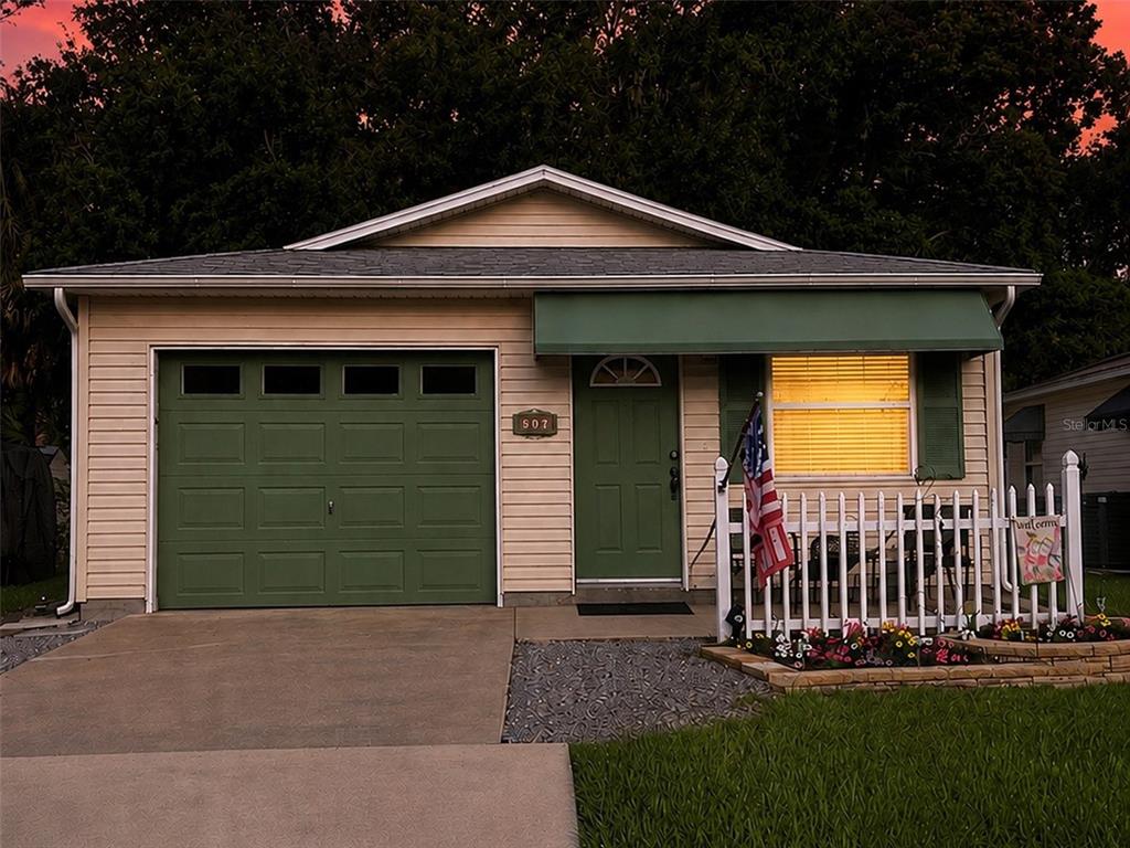 A small house exterior features light siding, green shutters, a green awning, and a white fence — 507 COTTAGE PARK LANE, LEESBURG, FL