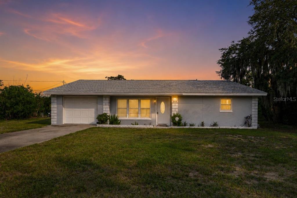 A single-story house with a light blue exterior, a concrete driveway, and two palm trees — 608 CHEROKEE CIRCLE, AVON PARK, FL