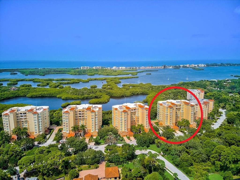 An aerial view shows several large residential buildings surrounded by lush greenery and coastal waters — 409 N POINT ROAD UNIT 803, OSPREY, FL