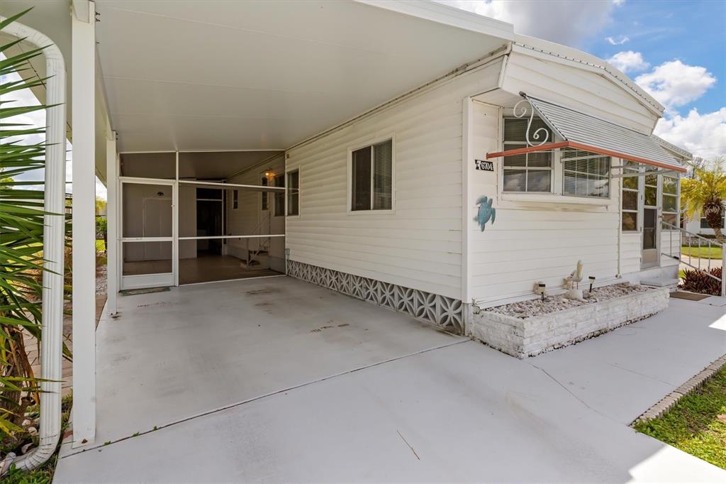 A white mobile home exterior features a covered carport, a screened entrance, and decorative siding — 6704 HOEMI COURT, NORTH PORT, FL