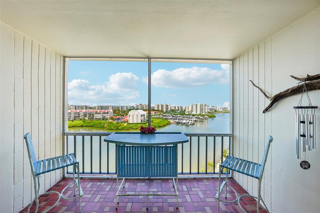 A screened-in balcony with a table, two chairs, and a view of a waterfront marina — 7400 SUN ISLAND DRIVE S UNIT 802, SOUTH PASADENA, FL