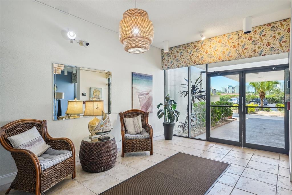 A bright lobby features wicker chairs, a patterned valance, and glass doors leading outside — 7400 SUN ISLAND DRIVE S UNIT 802, SOUTH PASADENA, FL