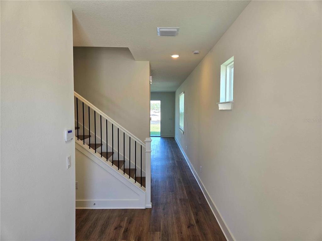 A hallway with wood-look flooring leads to a front door past a staircase with railings — 3819 DAYBREAK RUN LOOP, SPRING HILL, FL