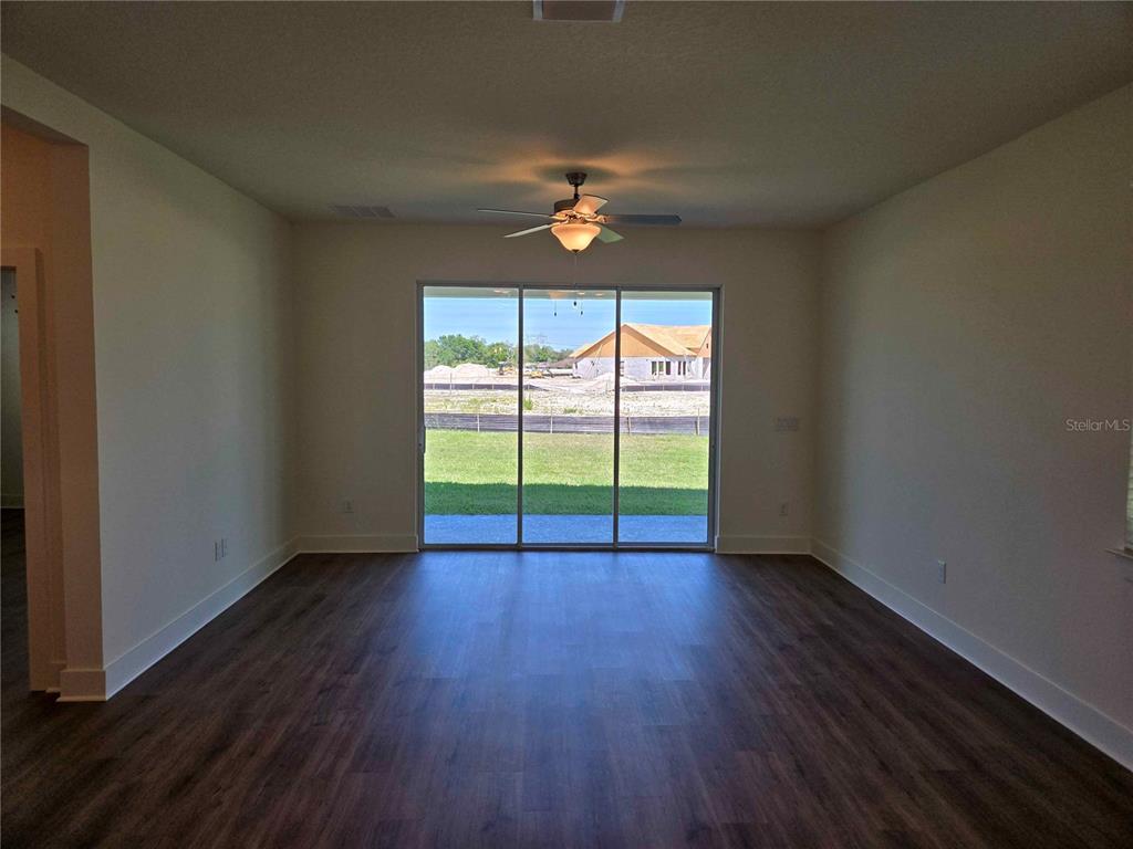 An empty room with dark wood-look flooring, a ceiling fan, and sliding glass doors — 3819 DAYBREAK RUN LOOP, SPRING HILL, FL