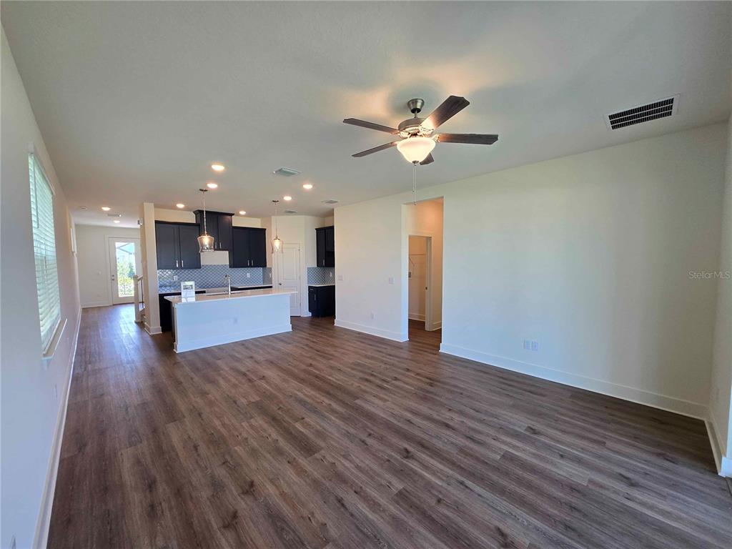 An open-concept living room features wood-look flooring, a ceiling fan, and an adjacent kitchen — 3819 DAYBREAK RUN LOOP, SPRING HILL, FL