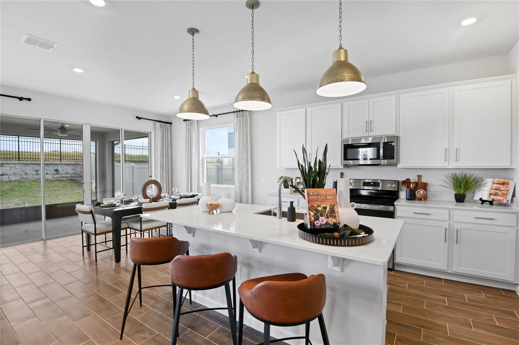 A modern kitchen features white cabinetry, a quartz island with bar stools, and tile flooring — 2230 ANDERS DRIVE, PARRISH, FL