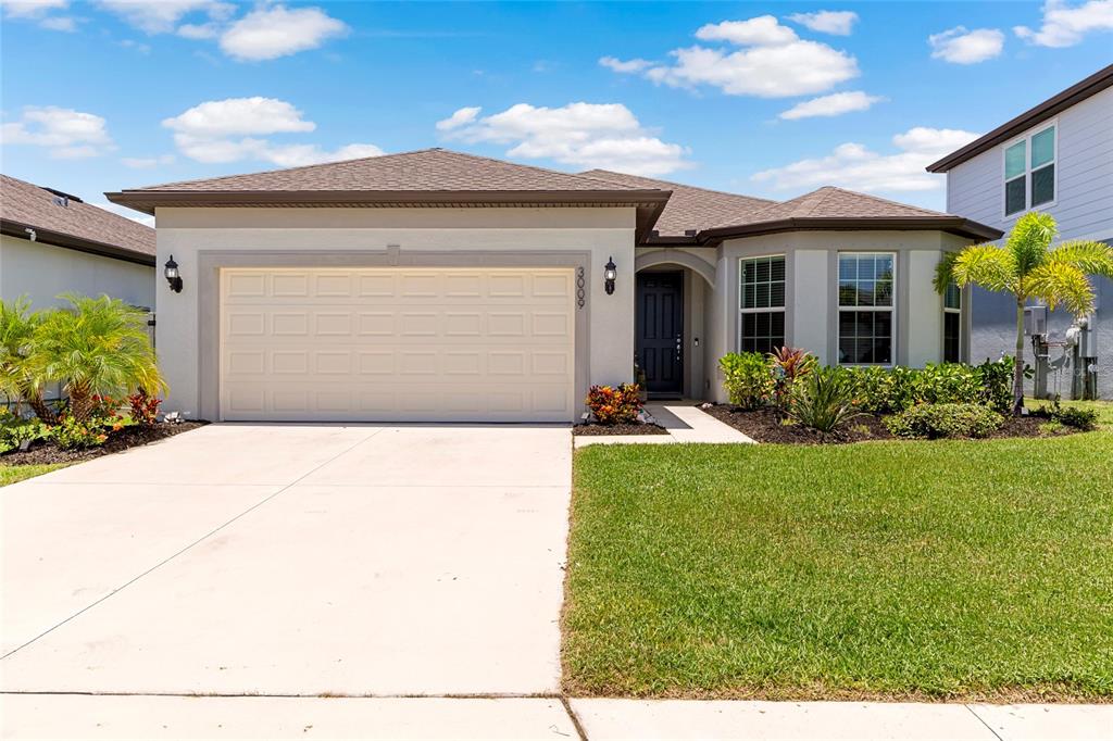 A single-story house with a beige stucco exterior, a two-car garage, and a landscaped yard — 3009 61ST DRIVE E, ELLENTON, FL