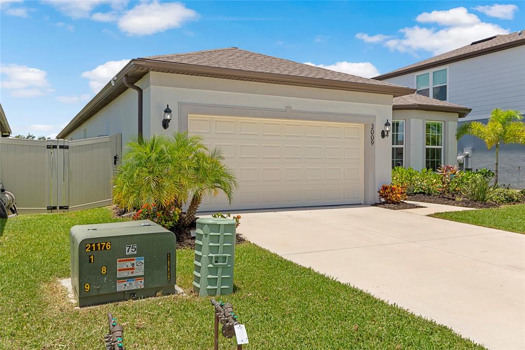 A single-story house exterior features a two-car garage, a driveway, and utility equipment in front — 3009 61ST DRIVE E, ELLENTON, FL