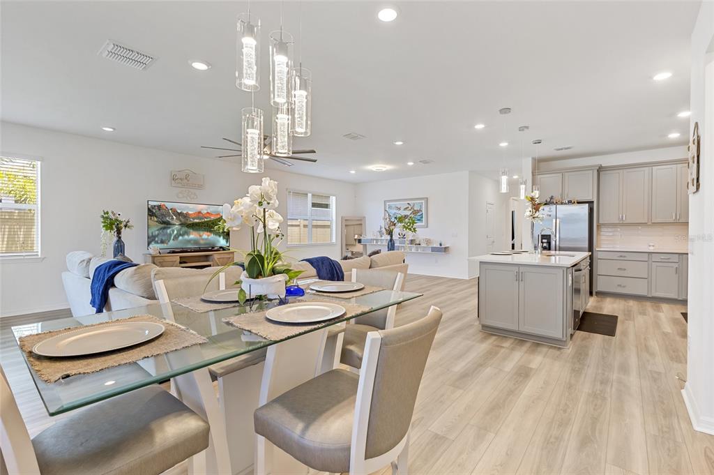 An open-concept living area features a glass dining table, a kitchen island, and light wood flooring — 3009 61ST DRIVE E, ELLENTON, FL
