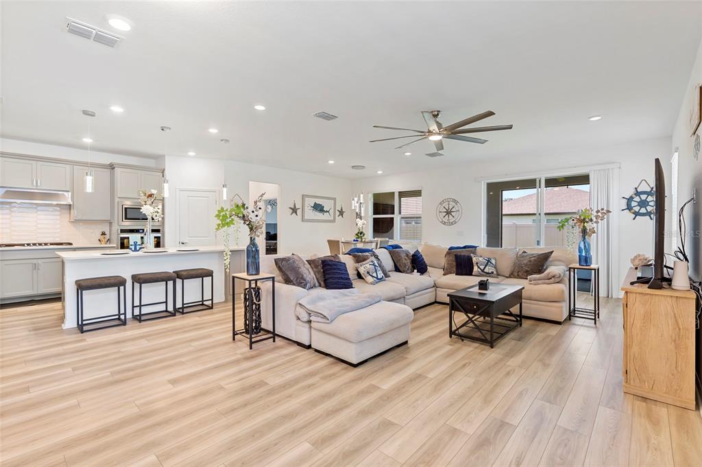 An open-concept living room and kitchen featuring light wood flooring and a large sectional sofa — 3009 61ST DRIVE E, ELLENTON, FL