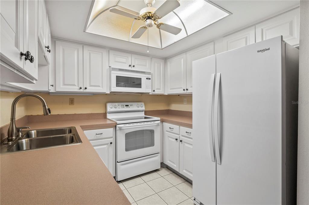 A kitchen with white cabinets, white appliances, a tan countertop, and a ceiling fan — 1609 WHITEBRIDGE DRIVE UNIT A, PALM HARBOR, FL