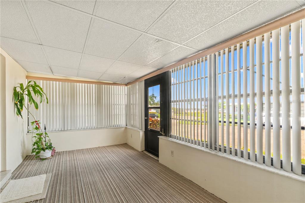 A sunroom features striped carpeting, a drop ceiling, and large windows covered by vertical blinds — 1609 WHITEBRIDGE DRIVE UNIT A, PALM HARBOR, FL