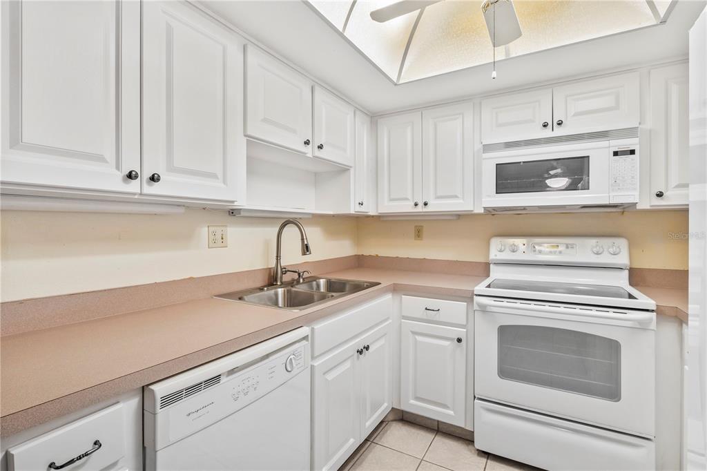 A kitchen features white cabinetry, a white stove, a dishwasher, and tan laminate countertops — 1609 WHITEBRIDGE DRIVE UNIT A, PALM HARBOR, FL