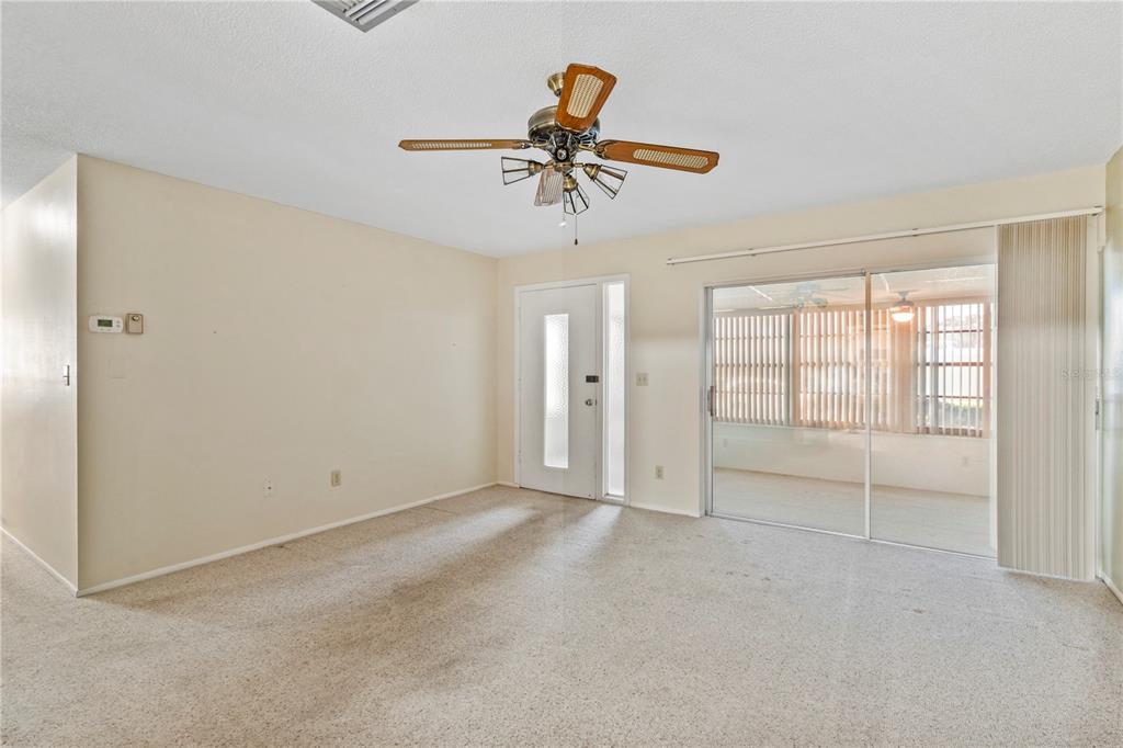 A living room features beige carpeting, a ceiling fan, a white door, and sliding glass doors — 1609 WHITEBRIDGE DRIVE UNIT A, PALM HARBOR, FL