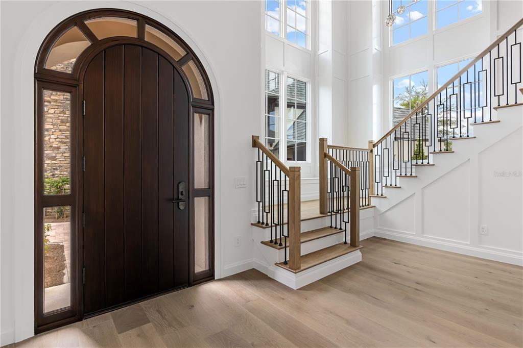 An entryway features a dark arched wooden door, light wood flooring, and a staircase with railings — 10331 WINTER SPARKLE CIRCLE, GOLDEN OAK, FL
