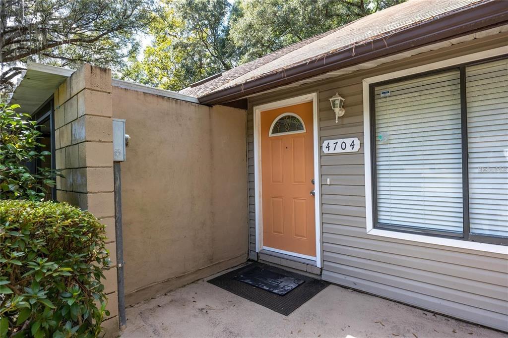 The exterior of a house features an orange front door, gray siding, and a concrete patio — 4704 SW 67TH TERRACE, GAINESVILLE, FL