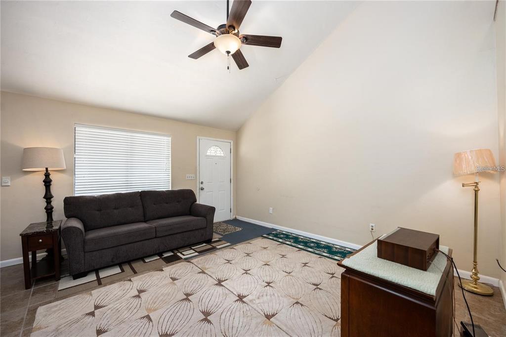 A living room features a dark sofa, a ceiling fan, and a patterned area rug — 4704 SW 67TH TERRACE, GAINESVILLE, FL