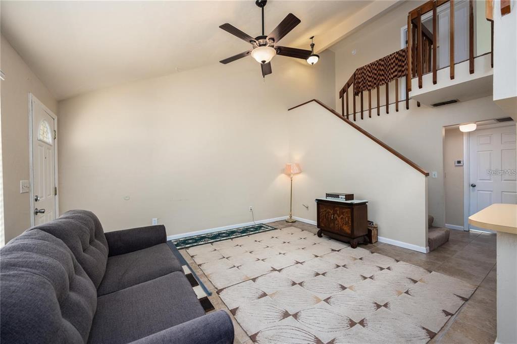 A living room with a vaulted ceiling, a ceiling fan, a staircase, and tile flooring — 4704 SW 67TH TERRACE, GAINESVILLE, FL