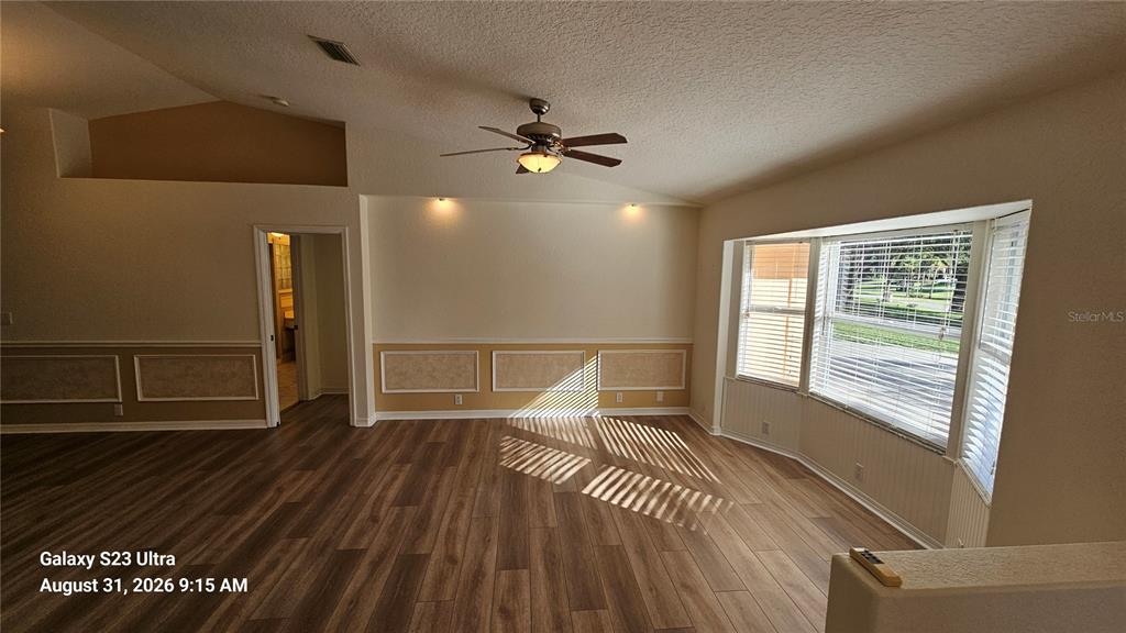 A living room with wood-look flooring, wainscoting, a ceiling fan, and a large bay window — 3998 DAKOTA CIRCLE, ORMOND BEACH, FL