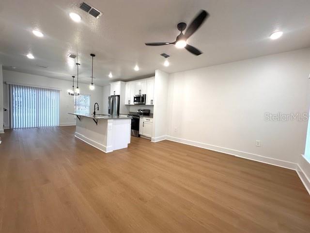 An open-concept kitchen with white cabinets and a center island overlooks a spacious living area — 250 E COLLINS STREET, UMATILLA, FL