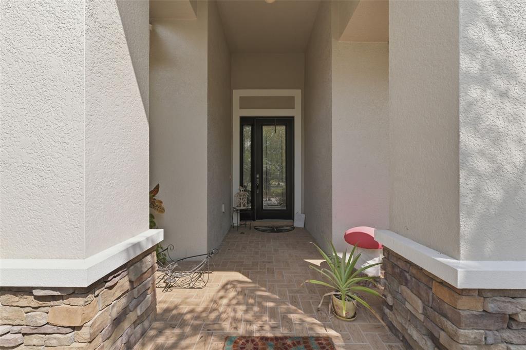 A covered entryway features a glass-paneled front door, stone-accented columns, and brick-patterned tile flooring — 2732 DEVONOAK BOULEVARD, LAND O LAKES, FL