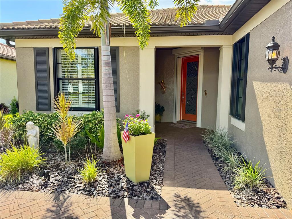 A paved walkway leads to the front entrance of a house with a bright orange door — 2436 ARUGULA DRIVE, NORTH PORT, FL
