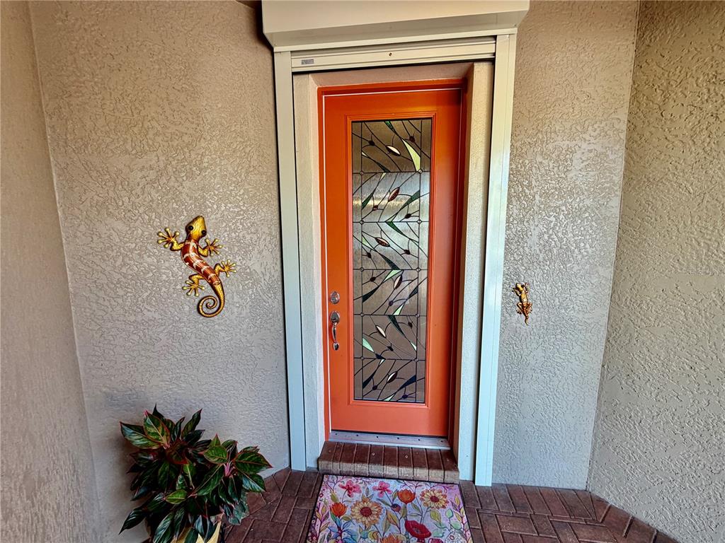 An orange front door with a stained glass insert is flanked by two lizard wall decorations — 2436 ARUGULA DRIVE, NORTH PORT, FL