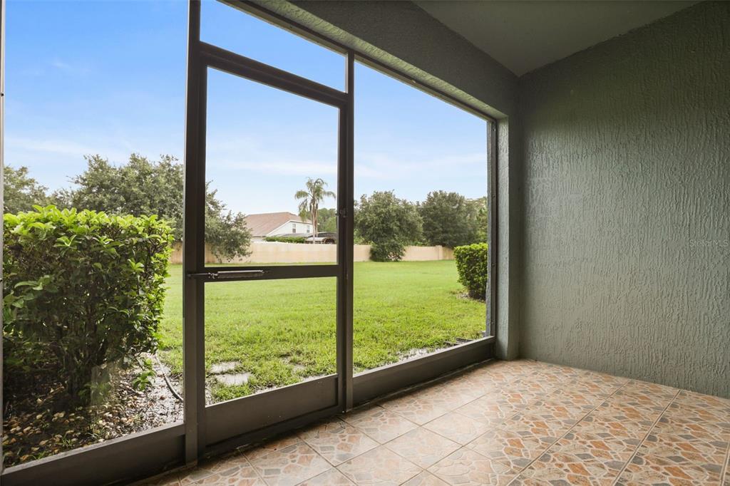 A screened-in patio with tiled flooring overlooks a grassy backyard with trees and a fence — 10332 MANDERLEY WAY UNIT 111, ORLANDO, FL