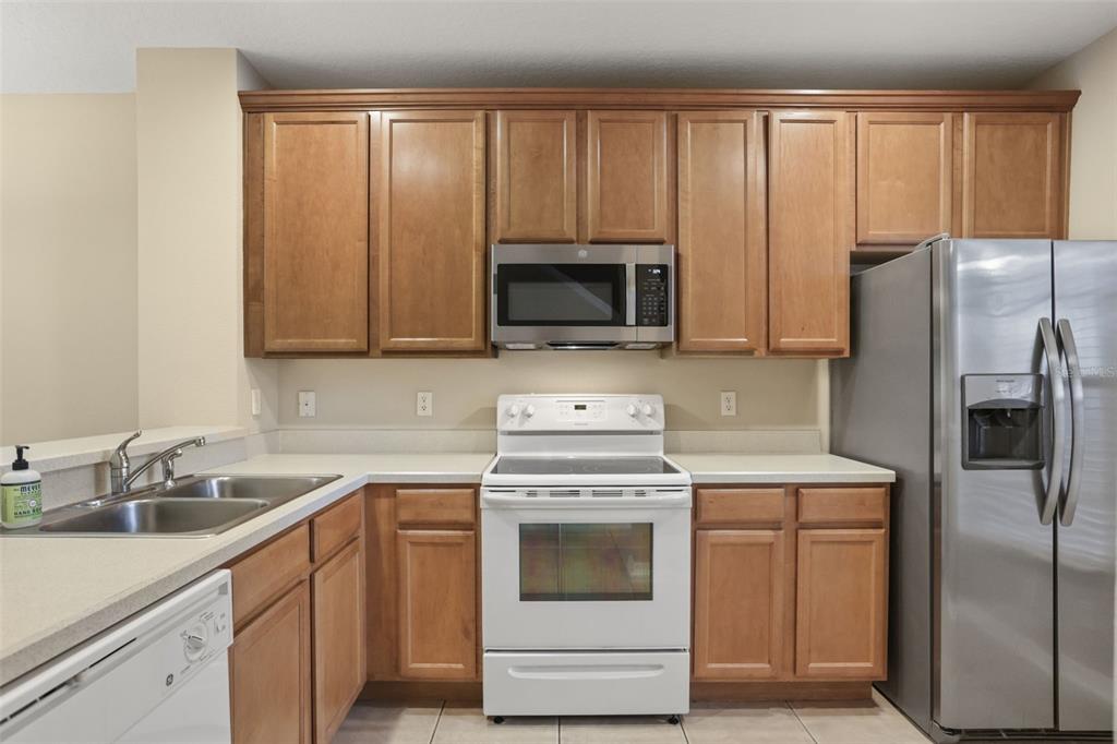 A kitchen featuring wood cabinets, white appliances, a stainless steel refrigerator, and light-colored countertops — 10332 MANDERLEY WAY UNIT 111, ORLANDO, FL