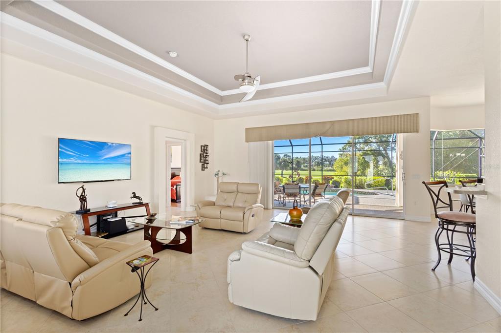 A living room with beige leather furniture, a tray ceiling, and sliding doors to a pool — 5283 PINE SHADOW LANE, NORTH PORT, FL