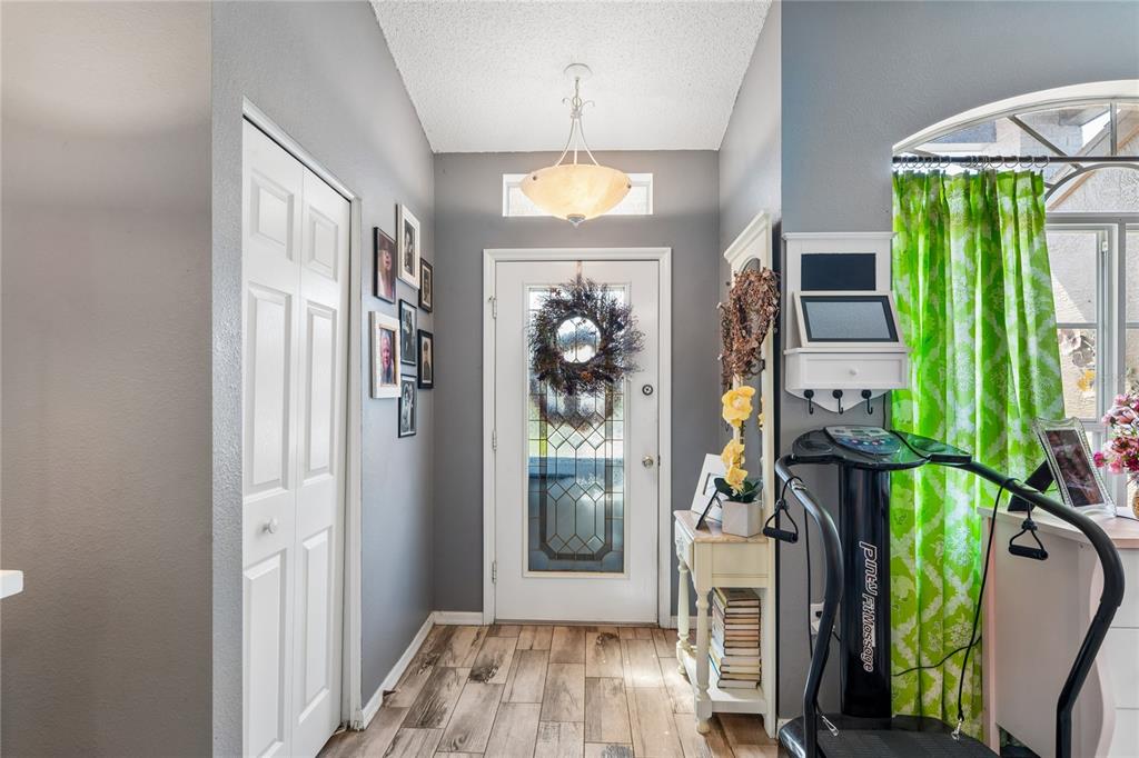 An entryway features gray walls, wood-look tile flooring, a white front door, and exercise equipment — 18607 BENT PINE DRIVE, HUDSON, FL