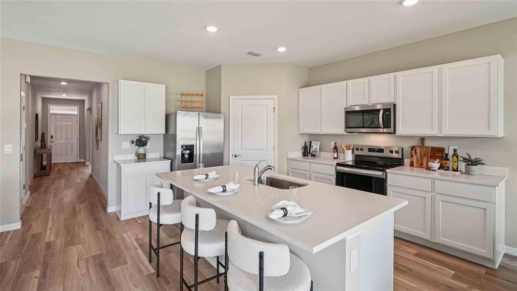 A modern kitchen features white cabinets, stainless steel appliances, a quartz island, and wood flooring — 24246 NW 13TH BOULEVARD, NEWBERRY, FL