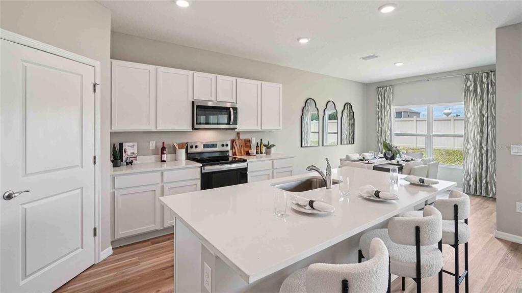 A modern kitchen features white cabinets, a large quartz island, and an adjacent dining area — 24246 NW 13TH BOULEVARD, NEWBERRY, FL