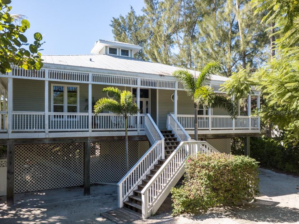 A stilt house with a wraparound porch, white railings, and a central staircase — 191 KETTLE HARBOR DRIVE, PLACIDA, FL