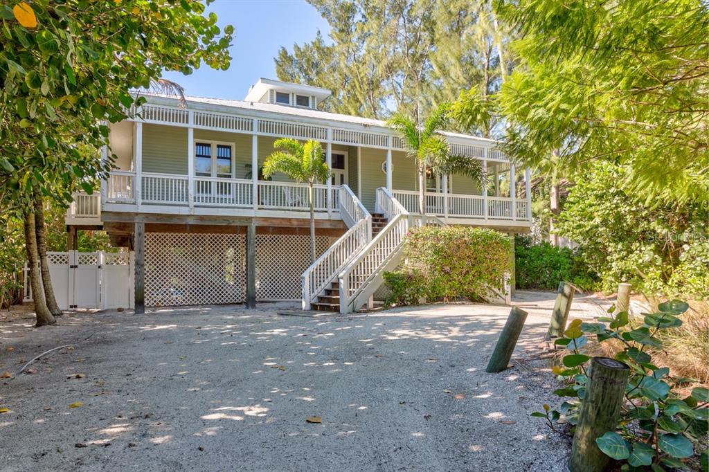 A raised, light green house with a wraparound porch and lattice skirting sits on sand — 191 KETTLE HARBOR DRIVE, PLACIDA, FL