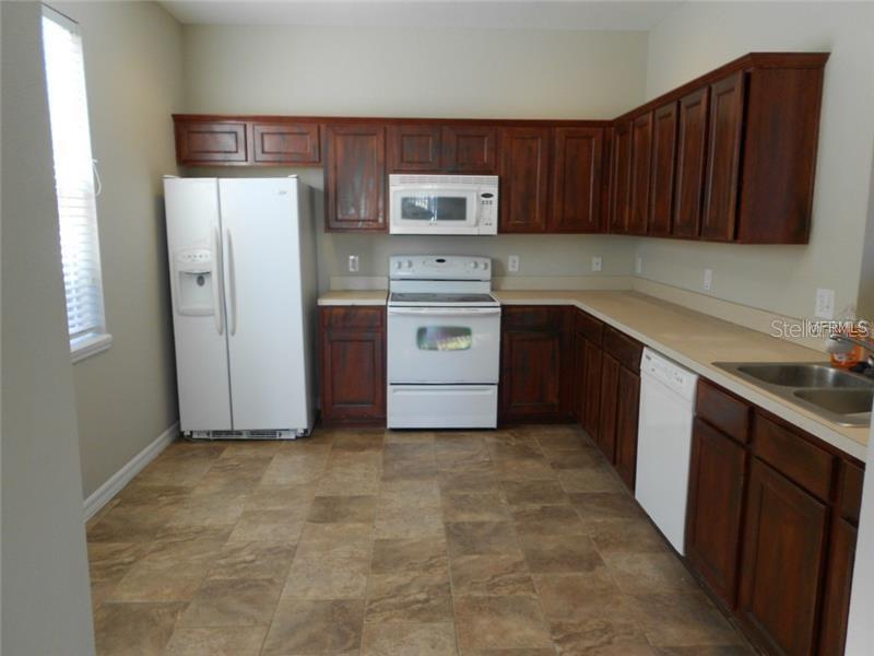 A kitchen features dark wood cabinets, white appliances, a double sink, and tiled flooring — 3911 PEMBERLY PINES CIRCLE, ST CLOUD, FL