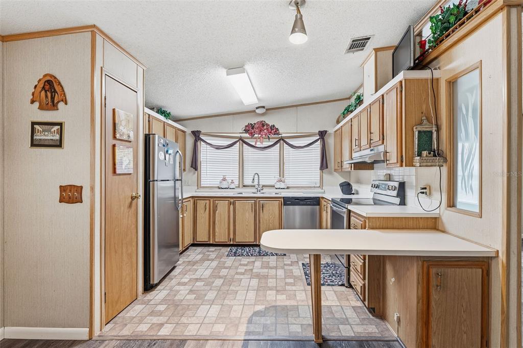 A kitchen features wood cabinets, stainless steel appliances, a peninsula counter, and tiled flooring — 410 DOLPHIN DRIVE S, OLDSMAR, FL